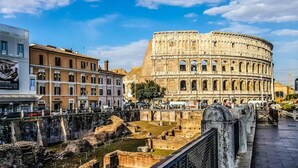A historic site with ancient ruins and a large amphitheater, surrounded by modern buildings. - Colosseo Rooms Imperial Rome (Rome)