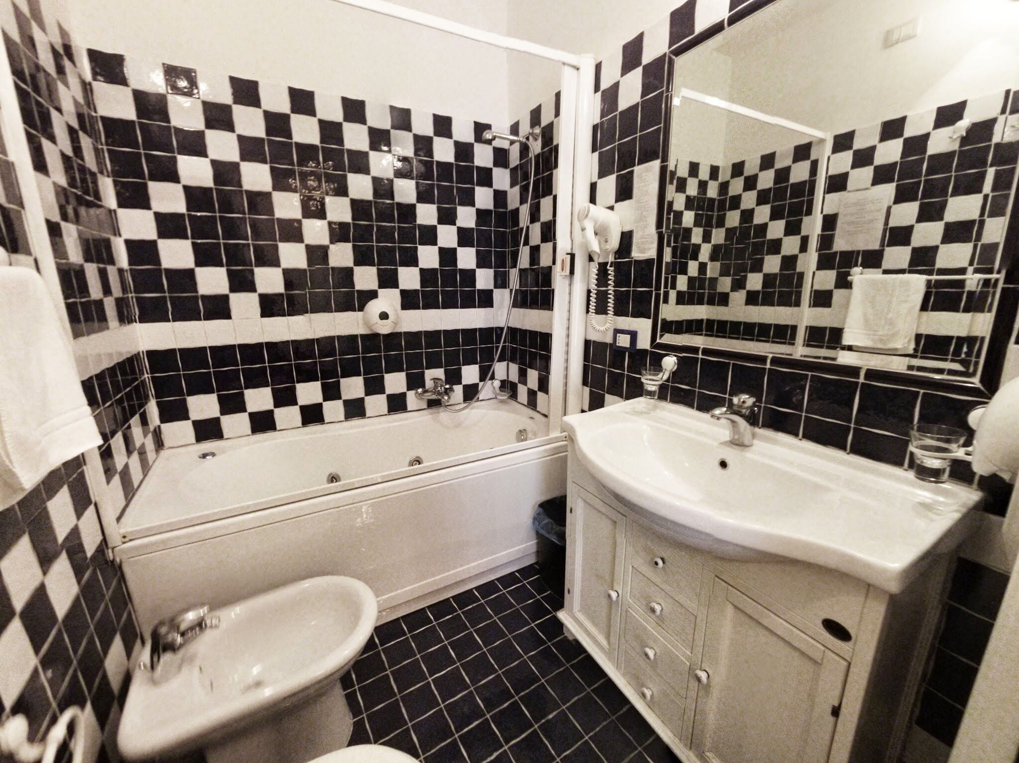 A bathroom with a checkered black and white tile pattern, a white bathtub, a sink, and a mirror.