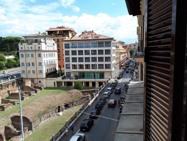 A street view with a mix of modern and historic buildings, a clear sky, and parked cars along the road.