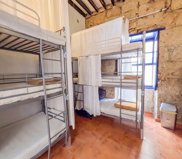 A dormitory room with bunk beds, a window with blue trim, and a trash bin. - Ashavana Nest Hostel (Granadilla de Abona)
