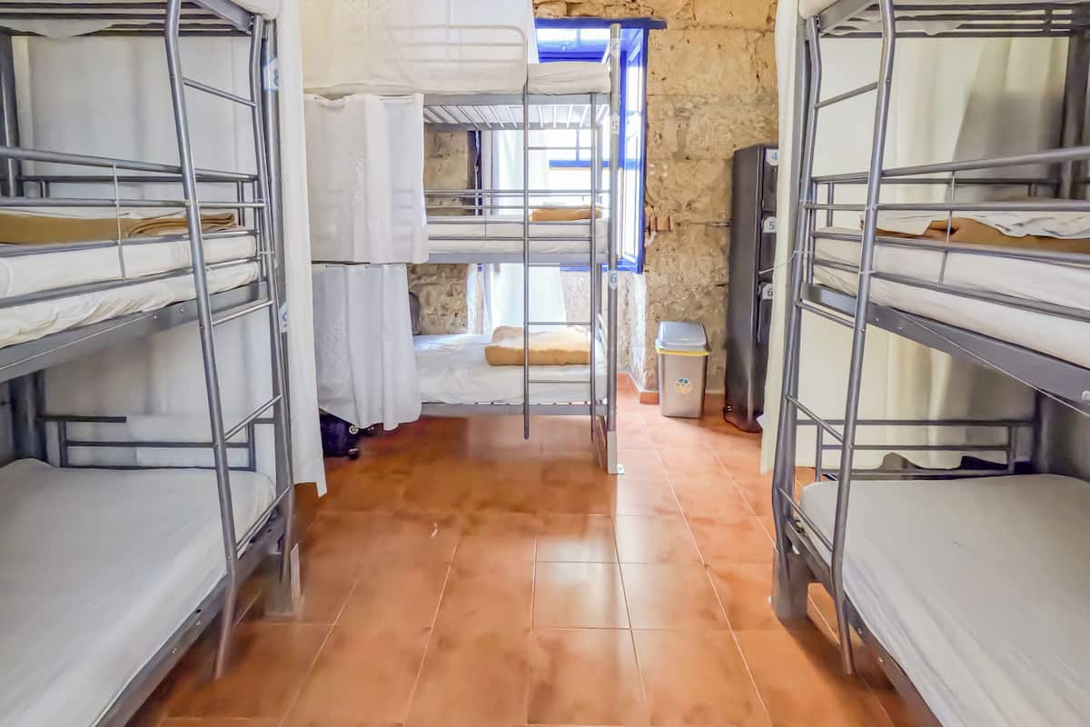A dormitory room with bunk beds, a window, and a tiled floor.