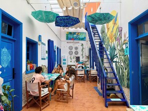 Una habitación con una escalera azul, una mesa con sillas y sombrillas colgando.