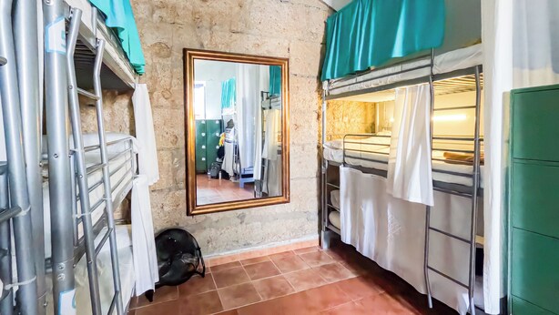 A narrow corridor with a stone wall, a mirror, and a bunk bed with a green cabinet. - Ashavana Nest Hostel (Granadilla de Abona)