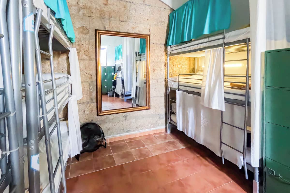 A narrow corridor with a stone wall, a mirror, and a bunk bed with a green cabinet.