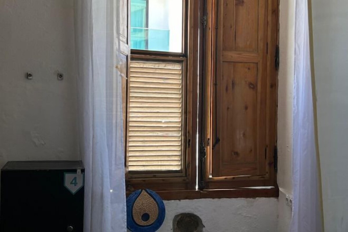 Un pasillo estrecho con una puerta de madera, una ventana con persianas y un pequeño adorno azul en la pared.