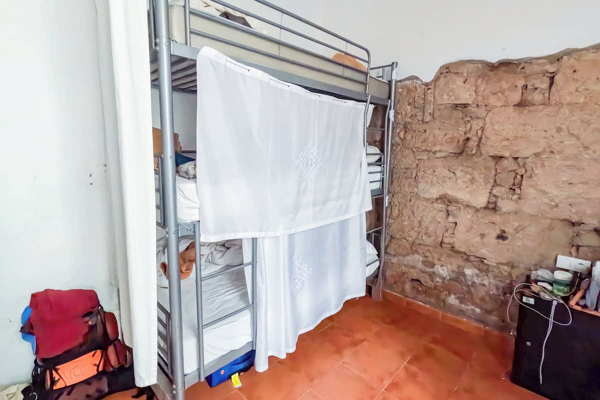 A bunk bed with a white curtain, a backpack, and a stone wall.