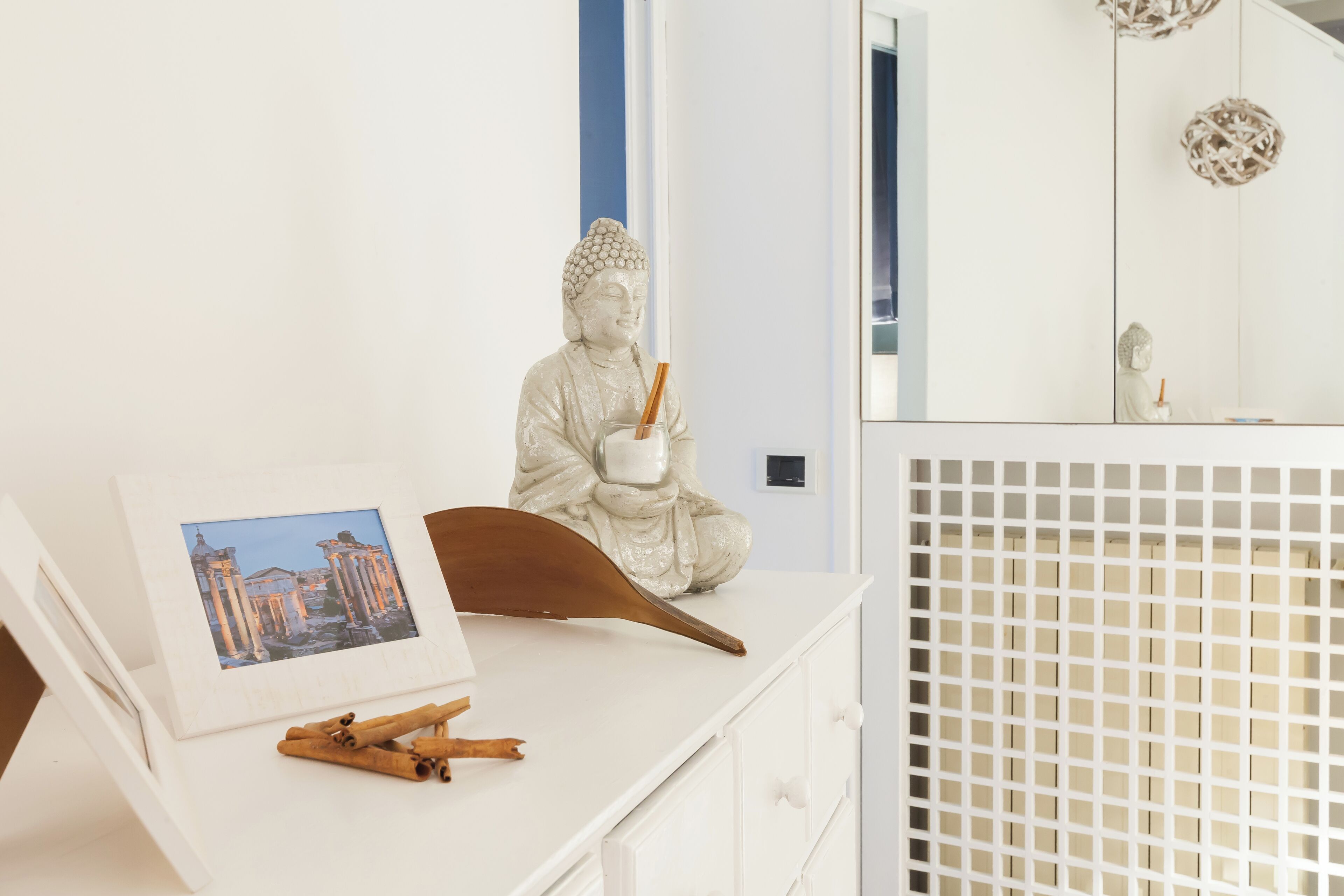 Et hvidt kommode med en Buddha-figur, en billedramme og en træske.