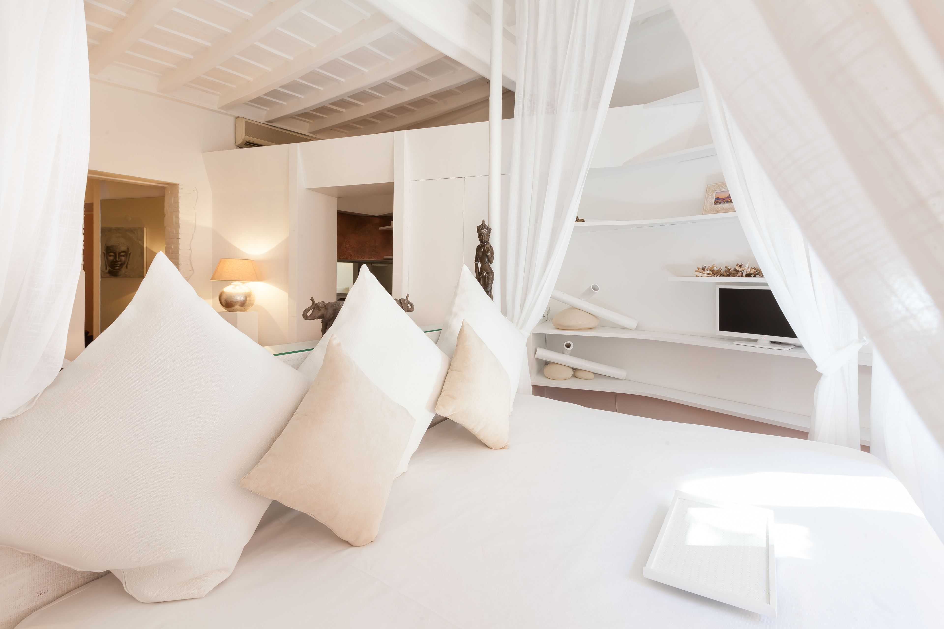 Un dormitorio con cama a dosel, ropa de cama blanca y una mesita de noche con lámpara.