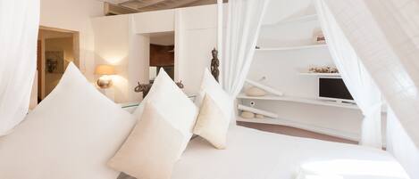 Un dormitorio con cama a dosel, ropa de cama blanca y una mesita de noche con lámpara.
