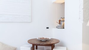 A round wooden table with a bowl of snacks, two white chairs, and a white cushioned bench. - Sweet Navona (Rome)