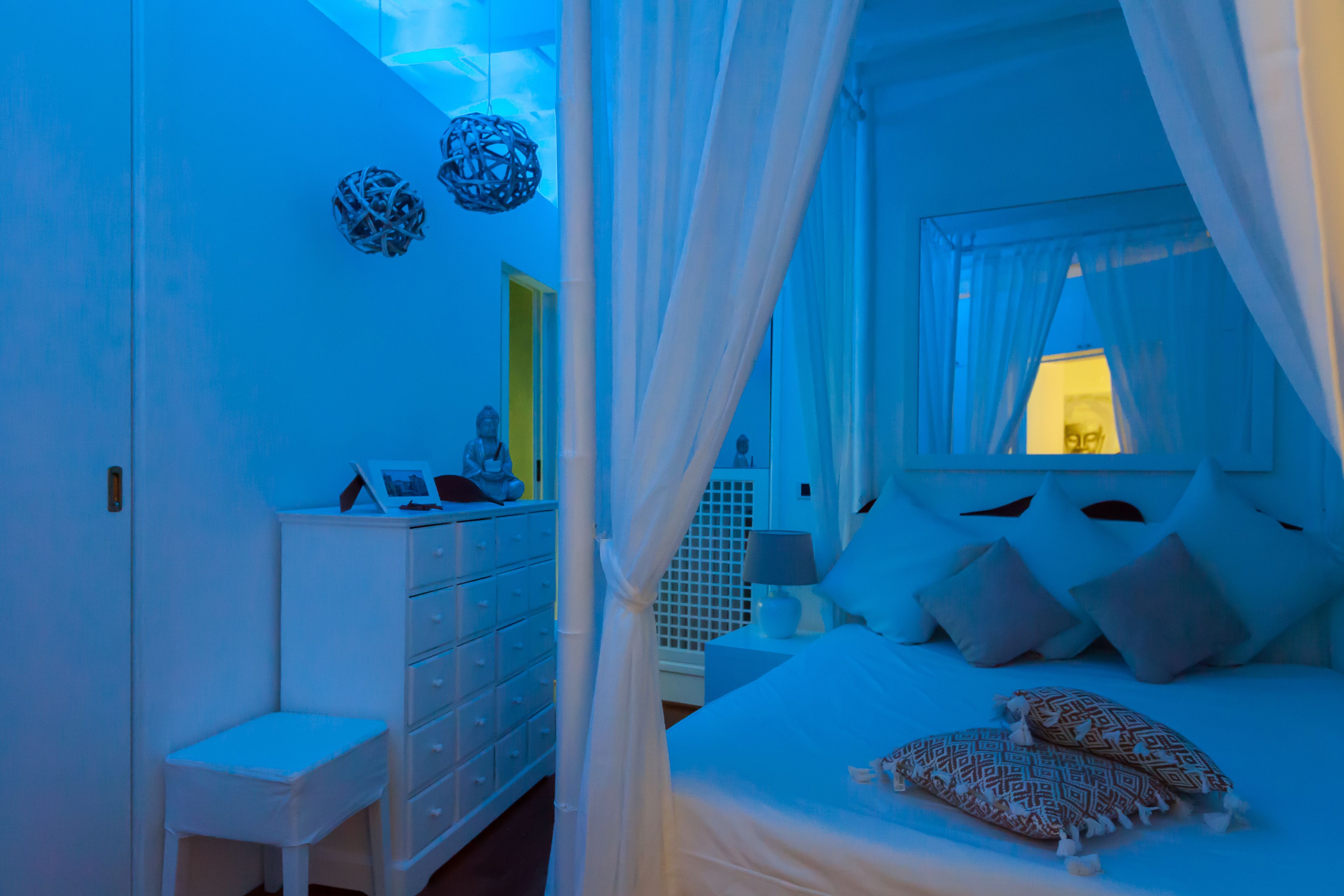 A bedroom with a canopy bed, a bedside table with a lamp, and a dresser.