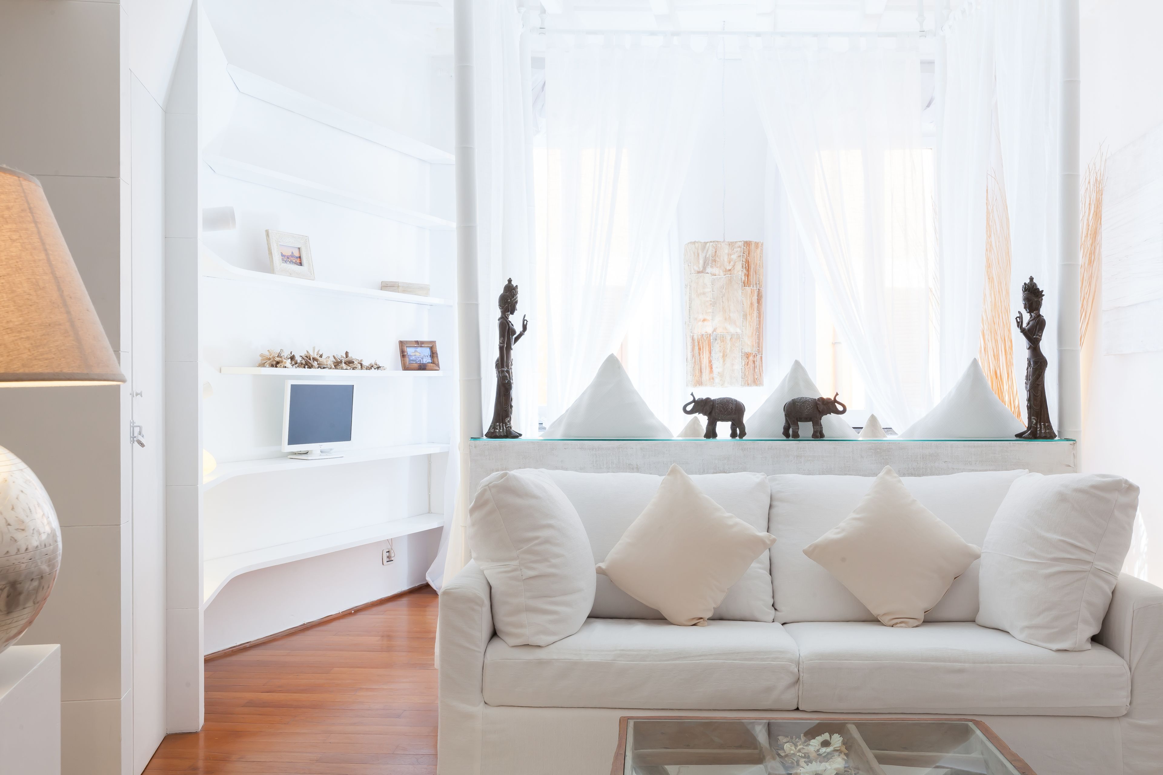 A modern living room with a white sofa, a glass coffee table, and a white TV on a stand.