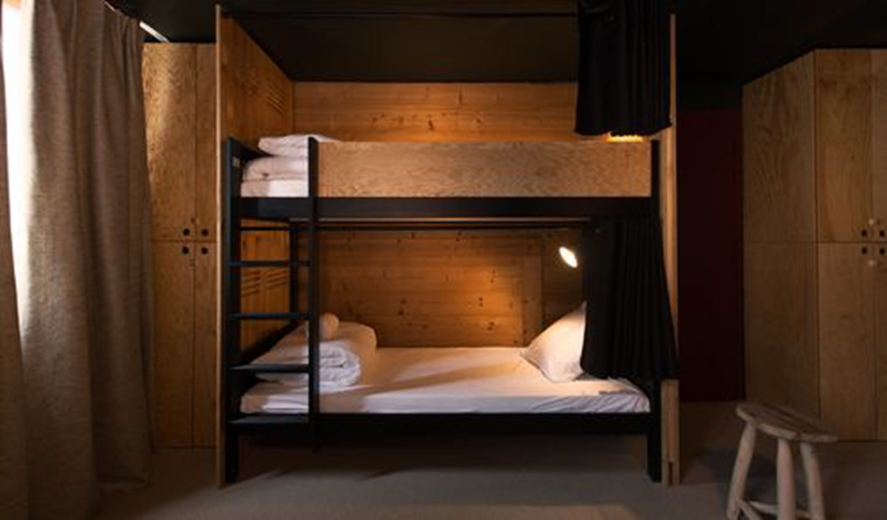 A bunk bed room with wooden walls and a single stool.