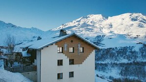 A snow-covered mountain with a building featuring a wooden facade and multiple windows. - Ho36 Les Menuires (Les Belleville)