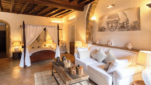 A bedroom with a four-poster bed, a white sofa, a wooden coffee table, and a Buddha painting on the wall. - Navona Deluxe Jolie (Rome)