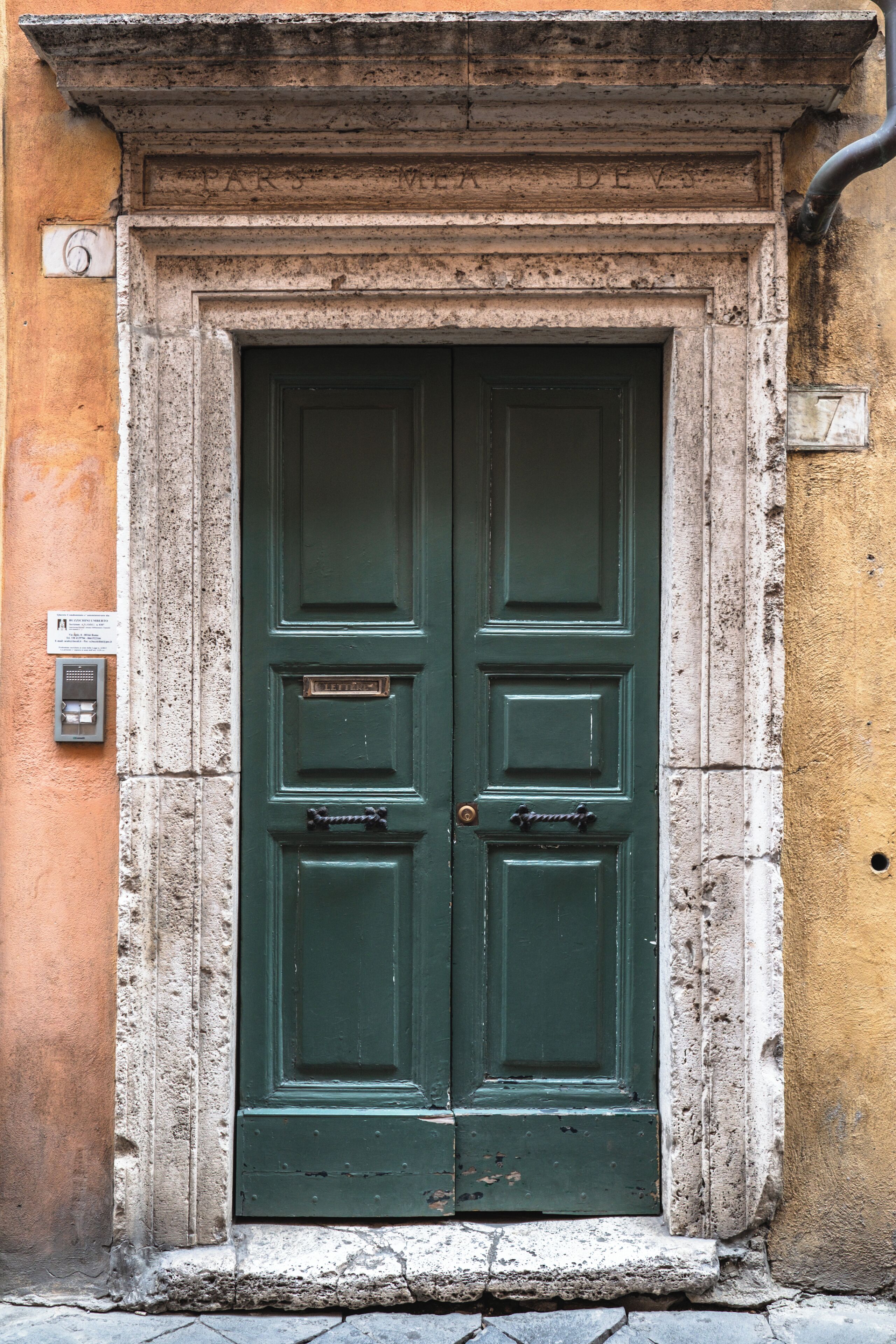 A green double door with a plaque, set in a stone frame, against a textured wall.