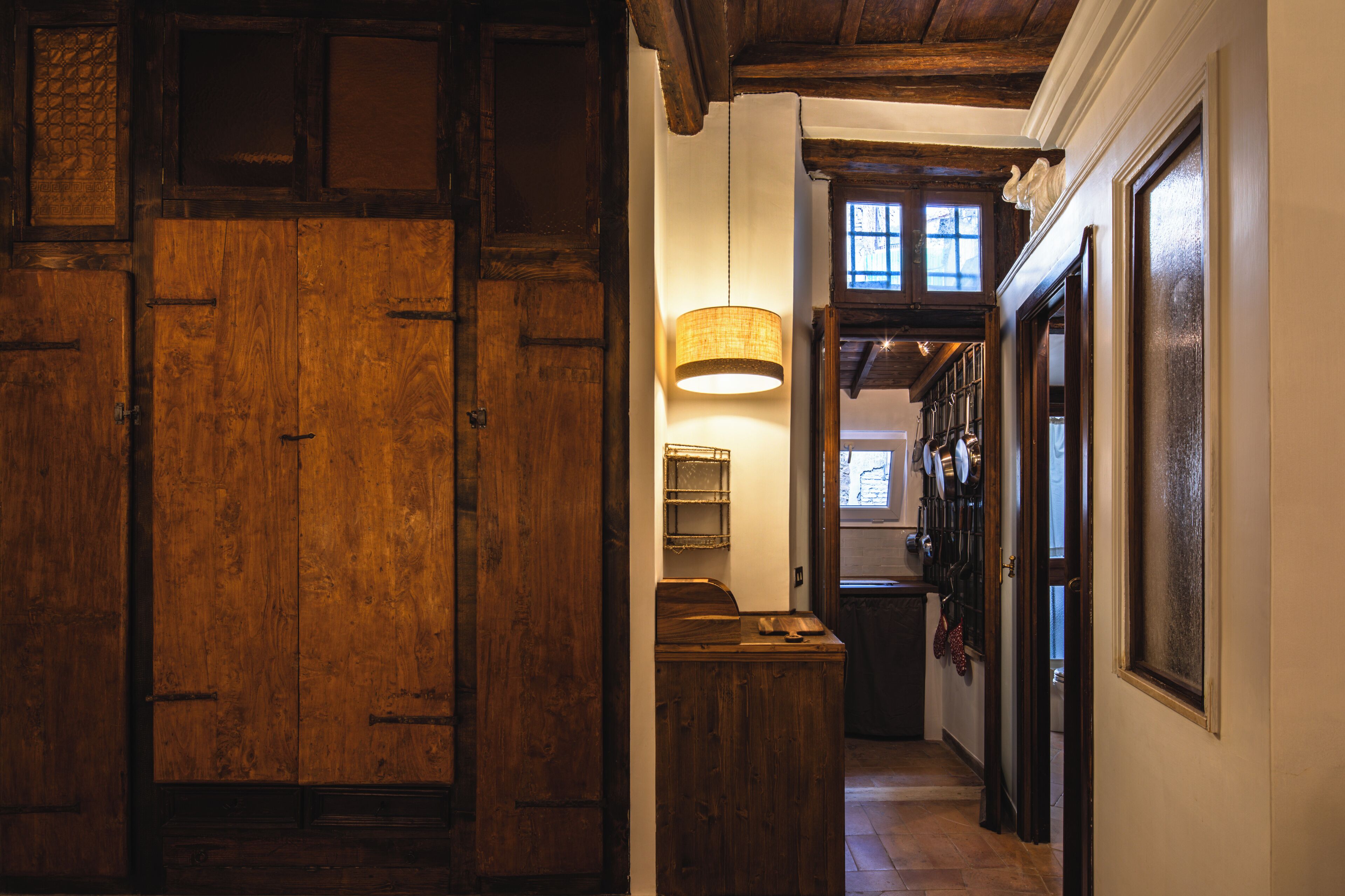 Un couloir en bois avec une lampe suspendue, une porte et une fenêtre donnant sur un paysage.