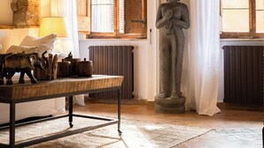 A room with a stone Buddha statue, wooden beams on the ceiling, a table with decorative items, and a window with wooden shutters. - Navona Deluxe Jolie (Rome)