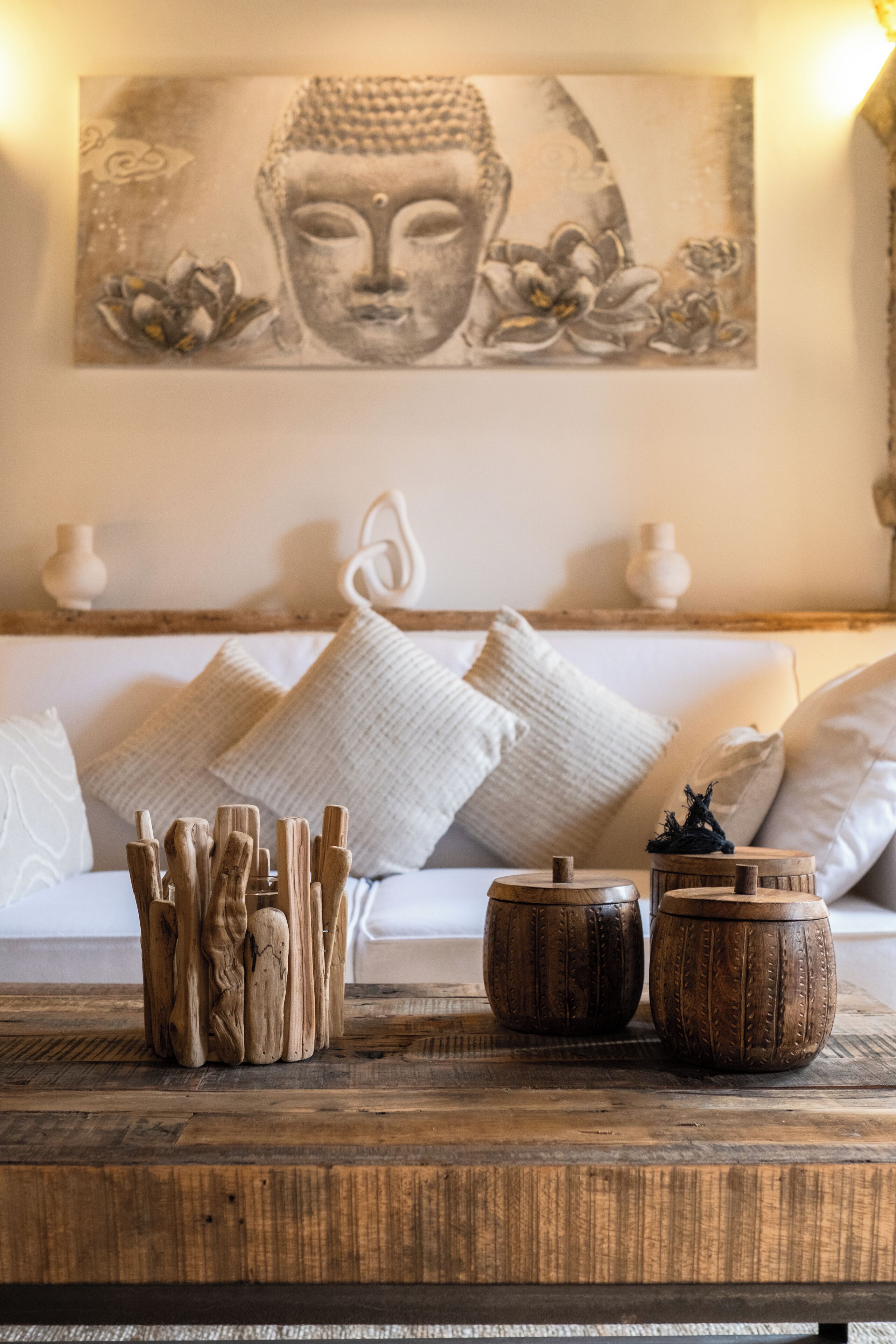 A room with a wooden coffee table, a Buddha painting, and a white sofa with cushions.