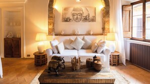 A cozy living room with a white sofa, a Buddha painting, and a wooden coffee table with decorative items. - Navona Deluxe Jolie (Rome)