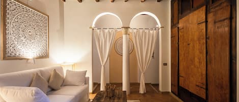 A room with a white sofa, a wooden table, a decorative wall piece, and a wooden wardrobe.