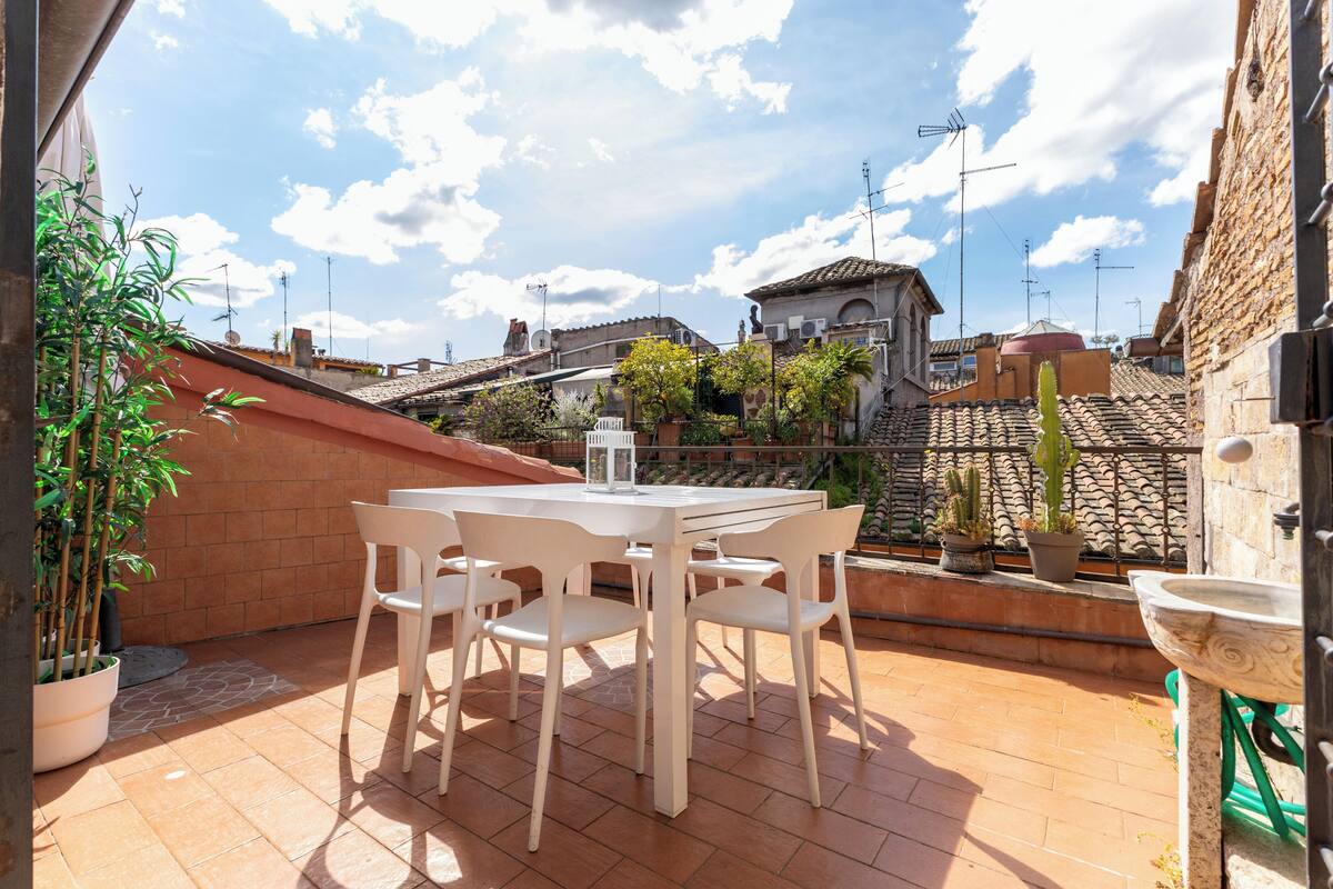 Un patio con una mesa y sillas, plantas en macetas y vistas de edificios al fondo.