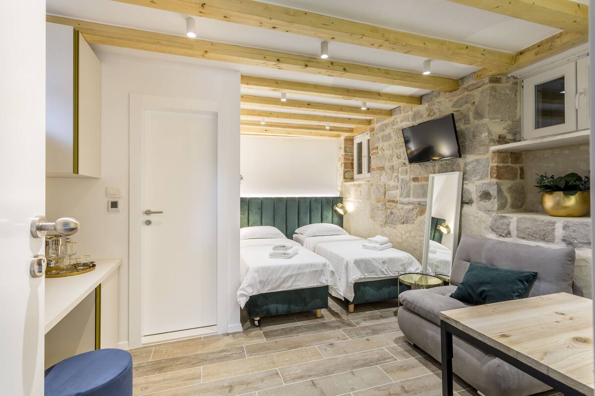 A modern room with two beds, a sofa, a wooden table, and a stone wall.