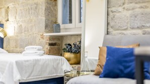 Ein Zimmer mit einem Bett, einem Sessel, einem kleinen Tisch und einem Fenster mit Blick nach draußen.