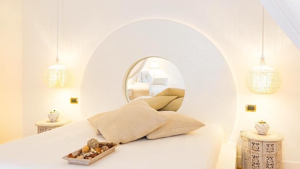 Un dormitorio con un espejo redondo grande, dos mesitas de noche con lámparas decorativas y una bandeja con frutos secos sobre la cama.
