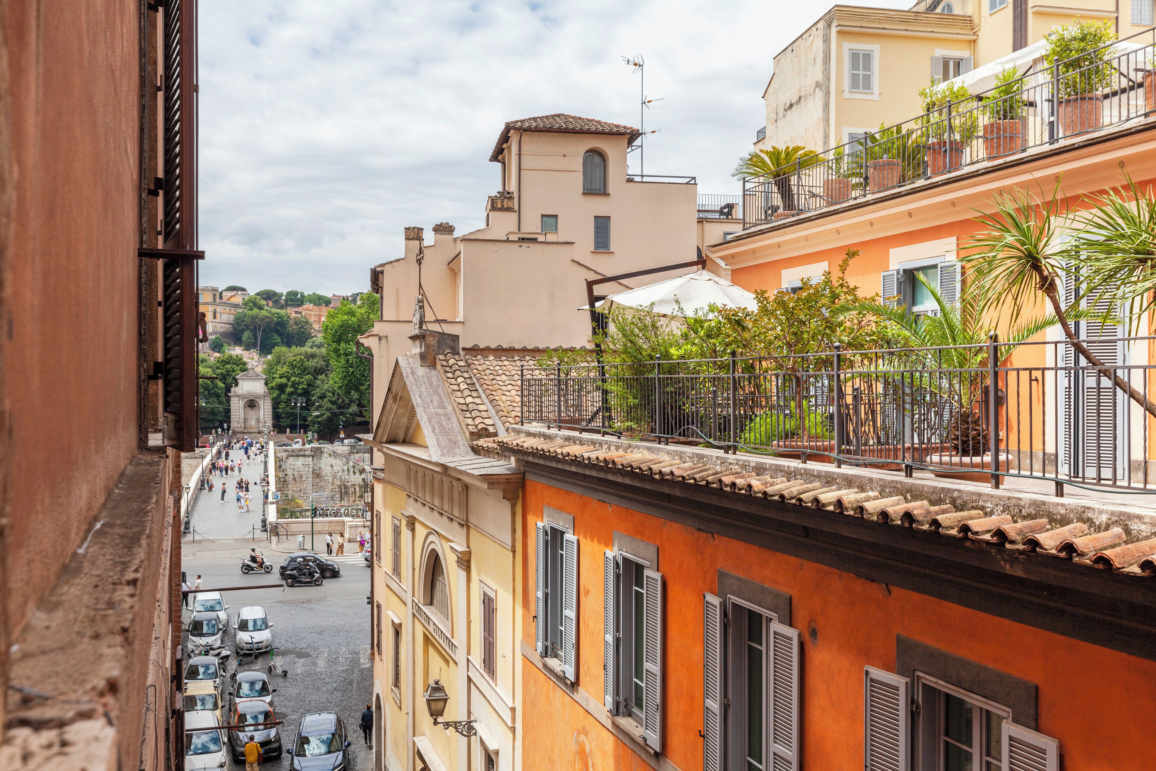 A narrow street with buildings on either side, balconies with plants, and a clear view of the street below.