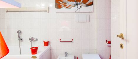 A bathroom with a bathtub, bidet, toilet, and a red towel.