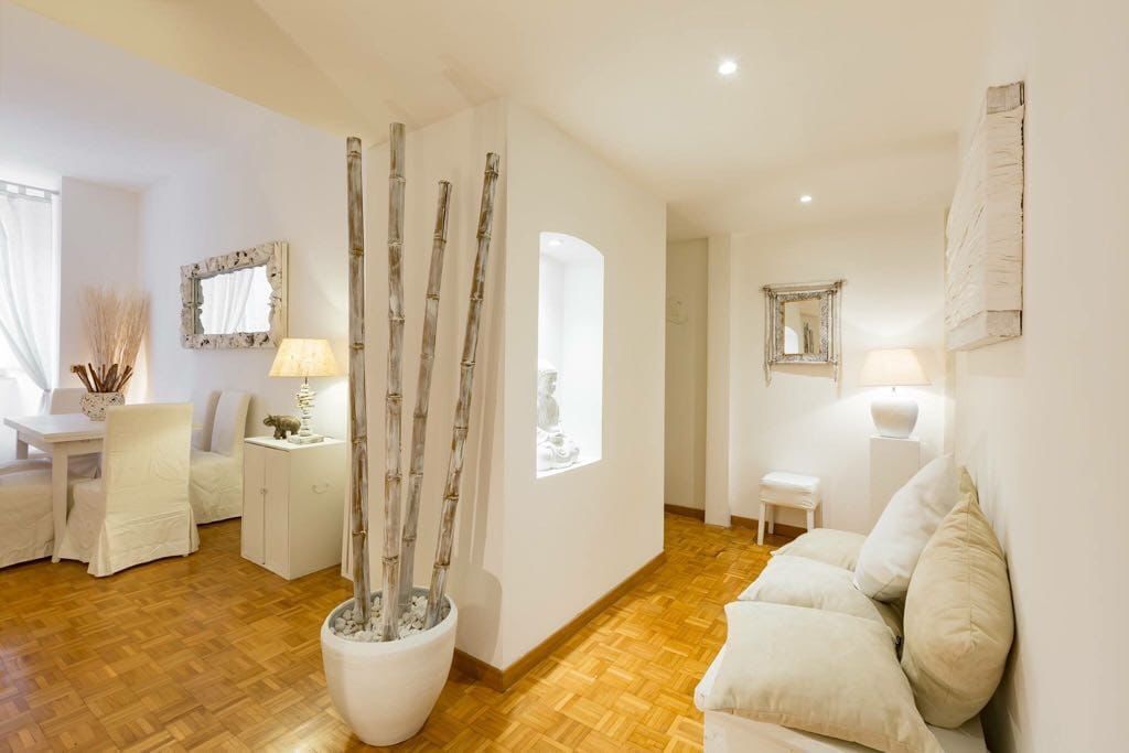 Un salon moderne avec un plancher en bois, des meubles blancs, une grande plante en pot et des miroirs décoratifs.