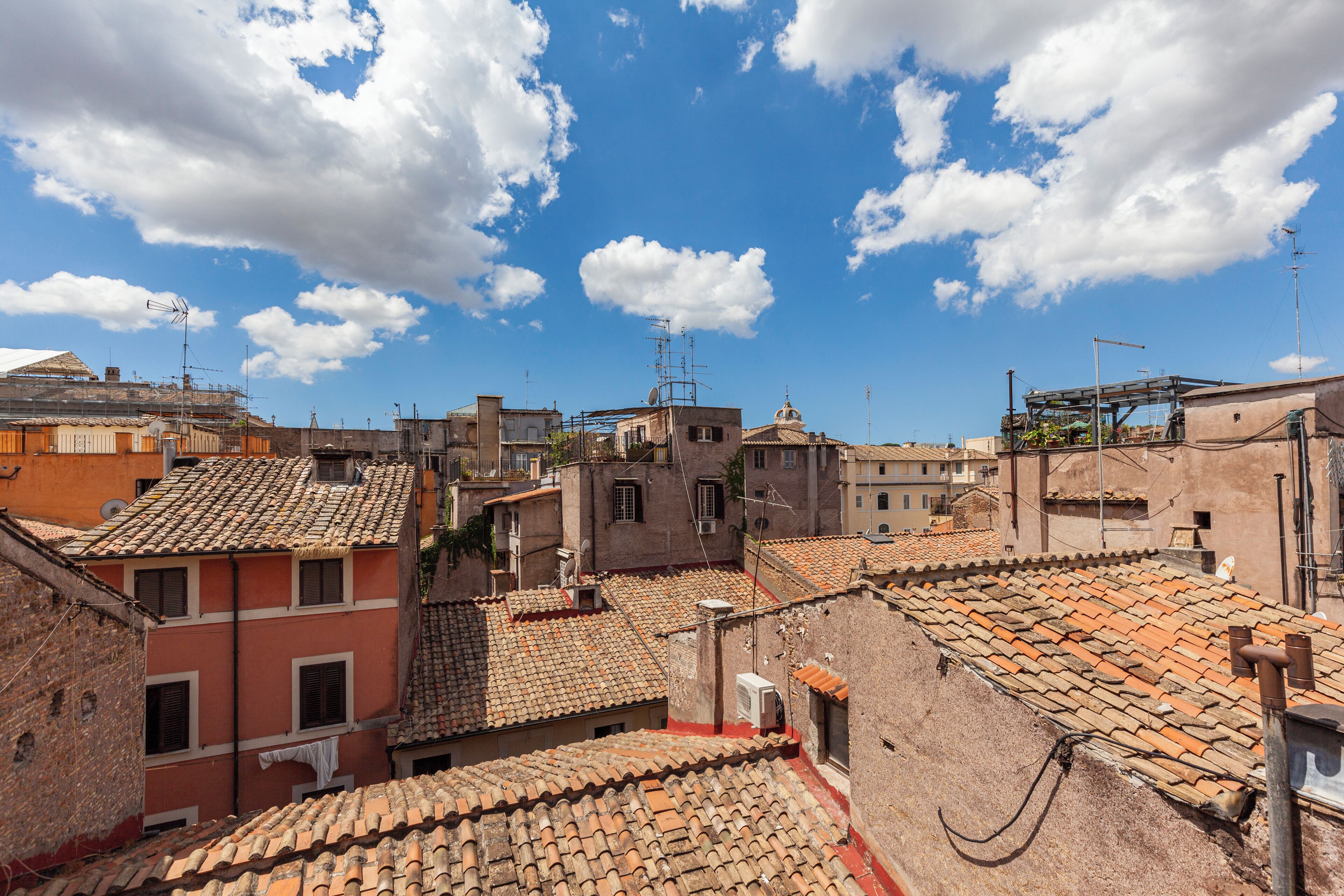 A view of a densely packed urban area with terracotta-tiled rooftops and various buildings, including some with domes and antennas.