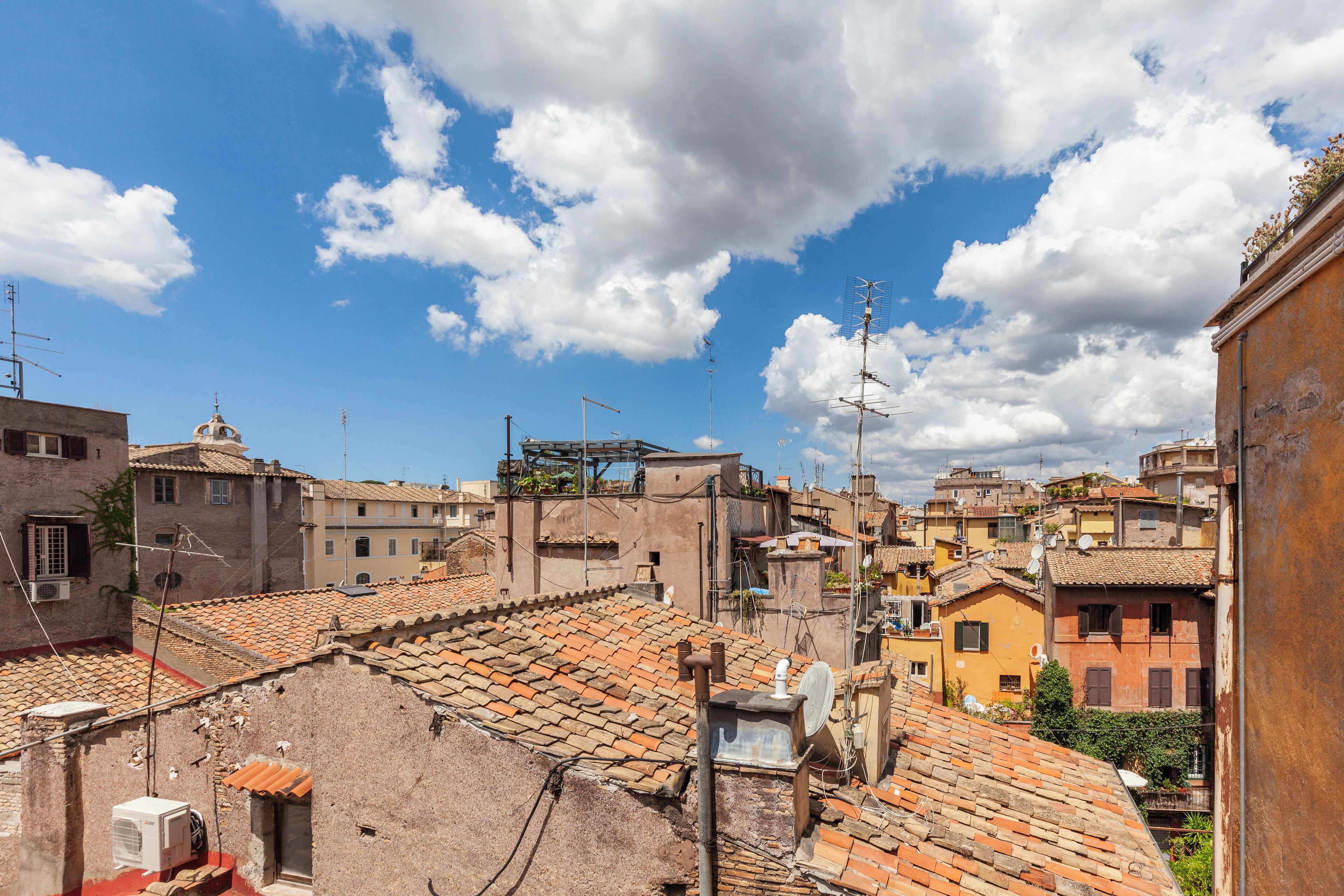A view of a densely packed urban area with terracotta-tiled rooftops and a variety of building styles, including some with domed roofs.