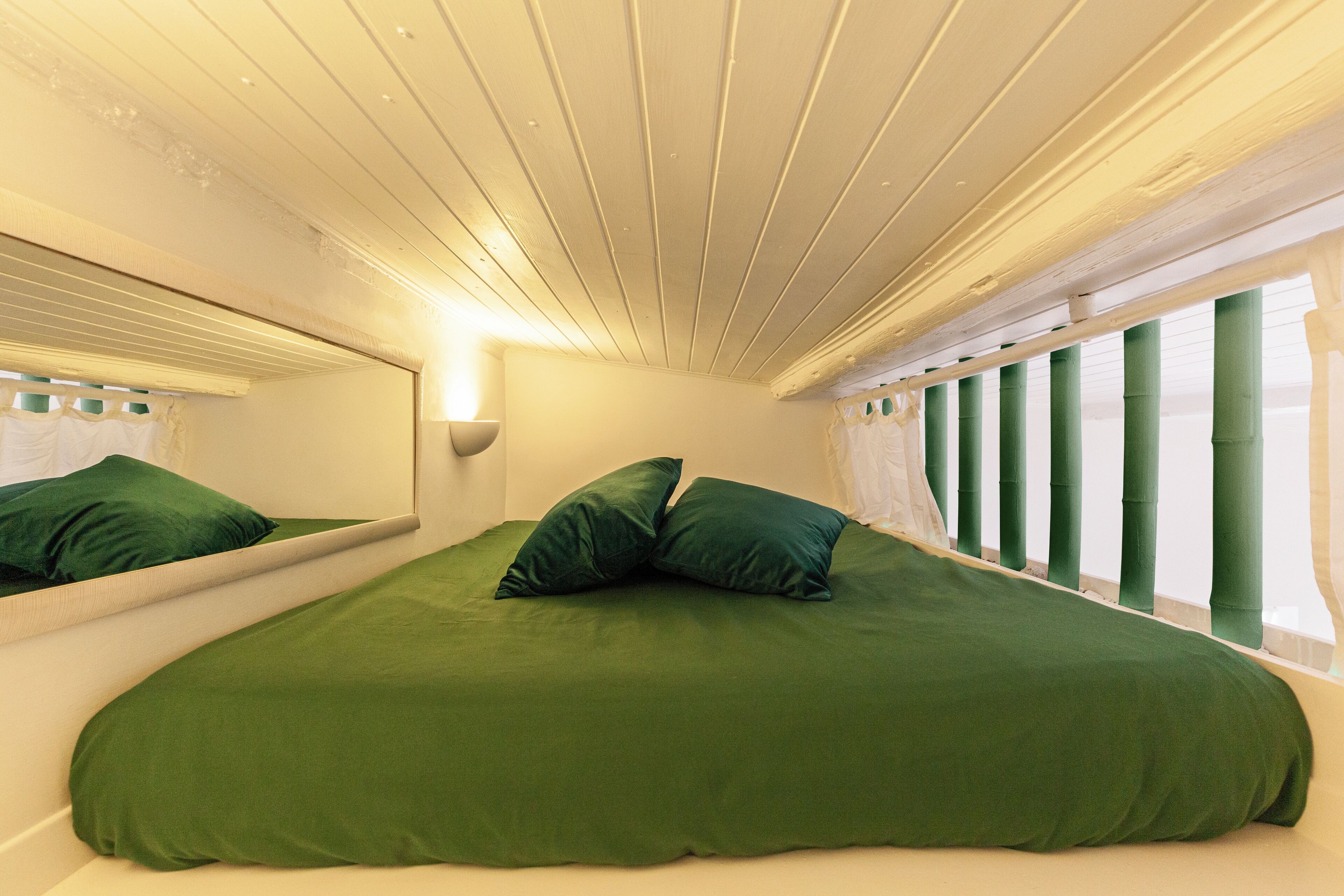 A room with a large bed, a mirror, and a window with green blinds.