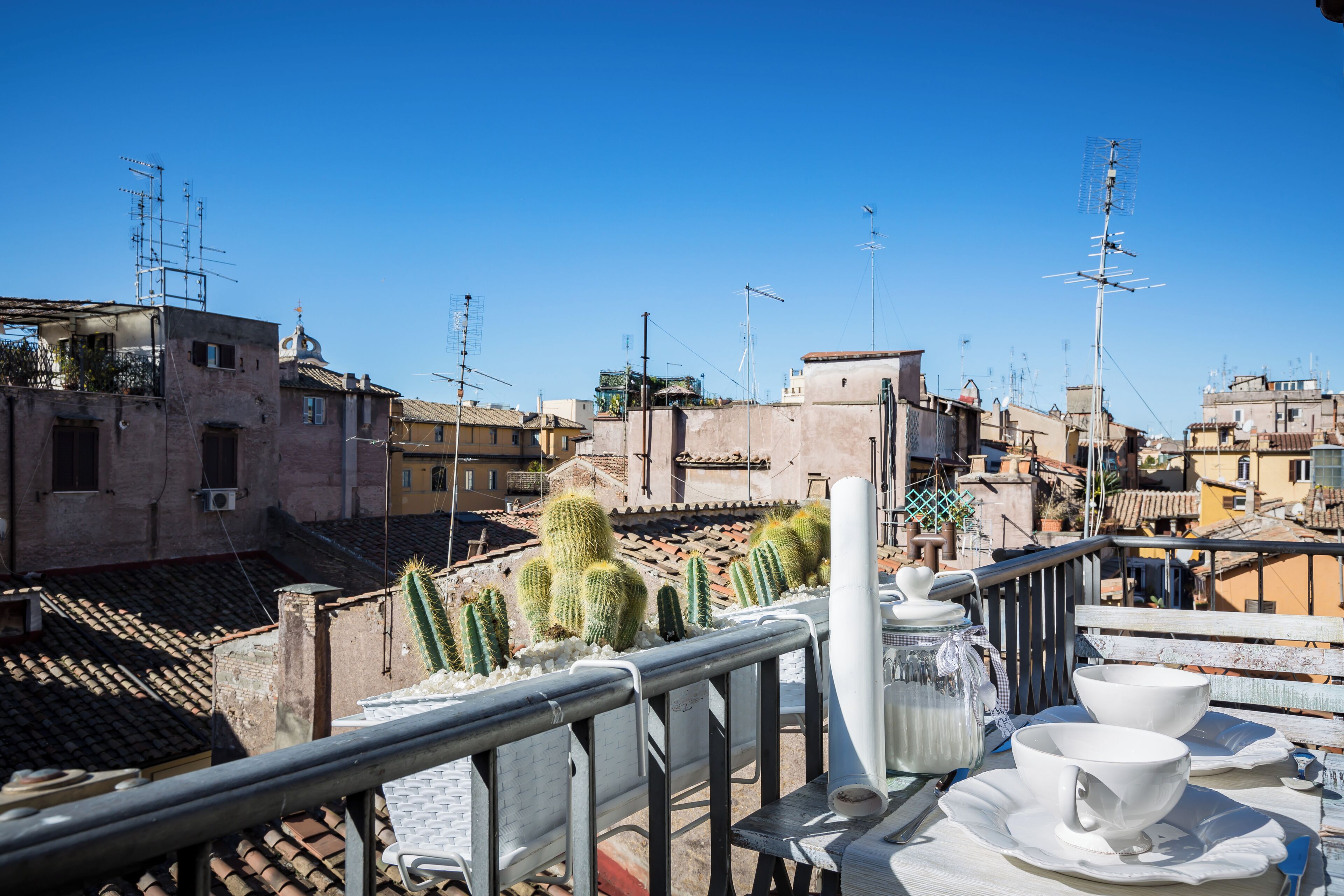 Terraza en la azotea con vistas panorámicas de la ciudad, con edificios, cactus y una barandilla de metal.