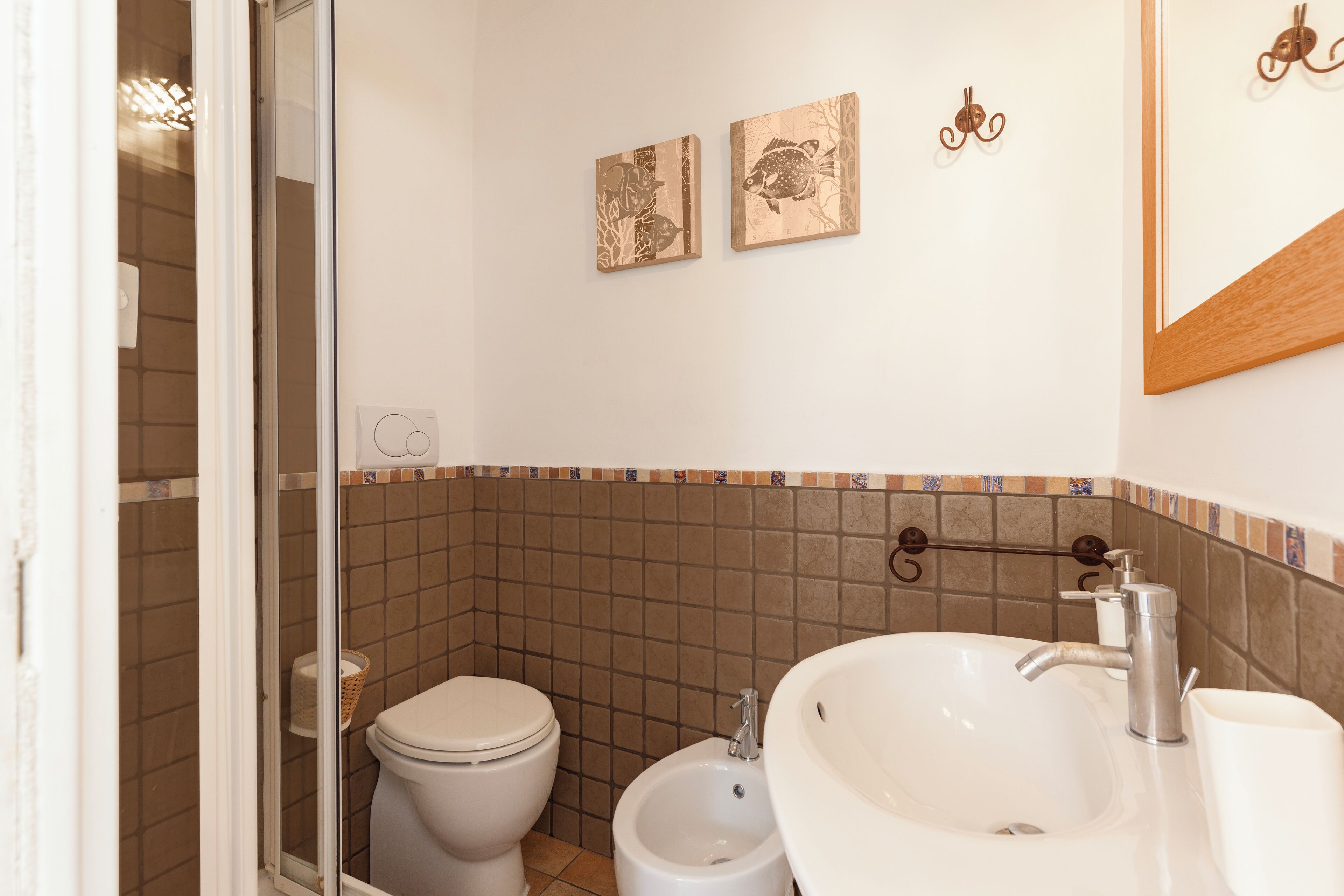 A bathroom with a toilet, bidet, and sink. There are two wall-mounted artworks and a mirror above the sink.