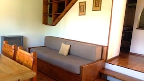 Ein Sofa aus Holz mit Kissen, ein Holztisch und eine Treppe, die in eine obere Ebene führt.