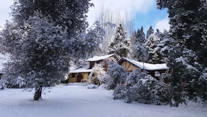 Een besneeerd landschap met een traditioneel houten huis, omringd door sneeuwzware bomen.