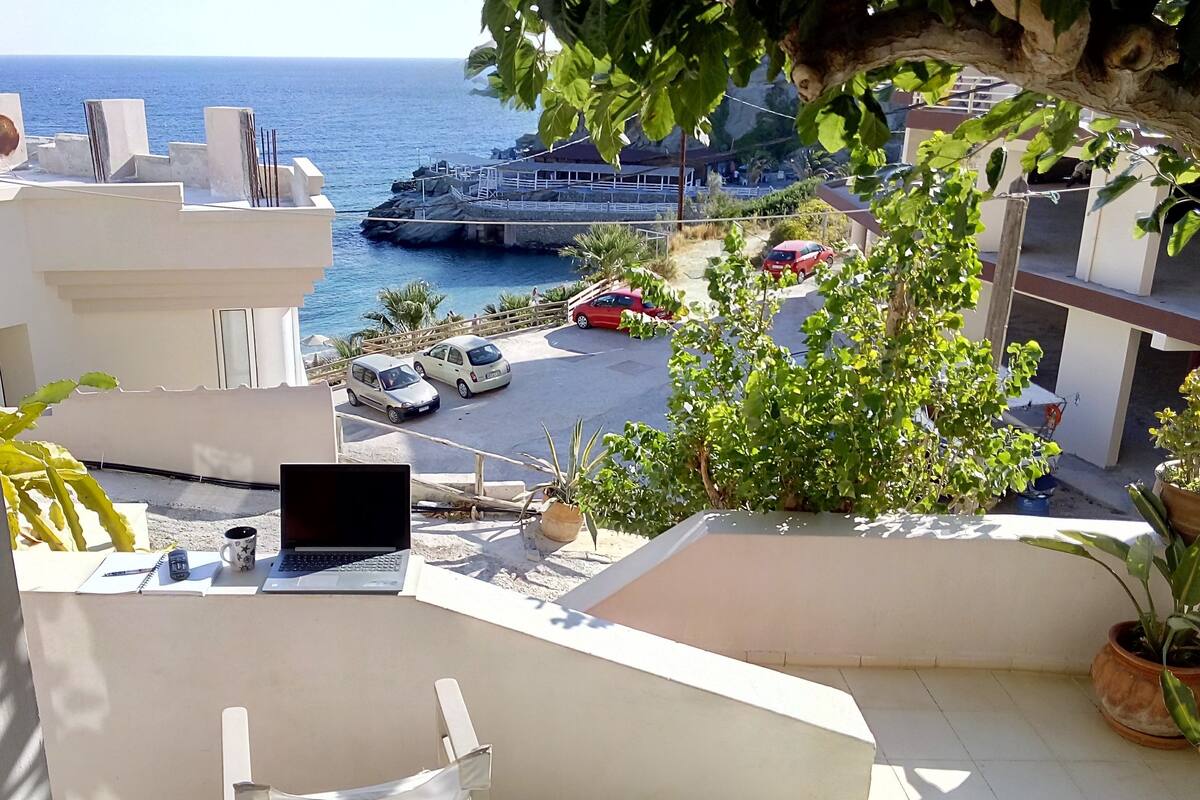 Ein Balkon mit Laptop, Notizbuch und Stift, der auf einen Parkplatz und den Küstenstreifen blickt.