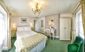 A hotel room with a bed, desk, chair, wardrobe, and chandelier.