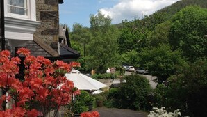 Un bâtiment en pierre avec une fenêtre blanche et, au premier plan, un jardin fleuri aux couleurs vives, notamment du rouge.