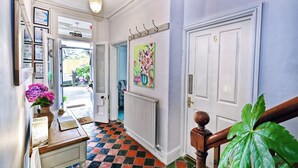 Un couloir avec un sol à carreaux, un radiateur, une porte dotée d’une poignée en laiton et une grande plante verte.