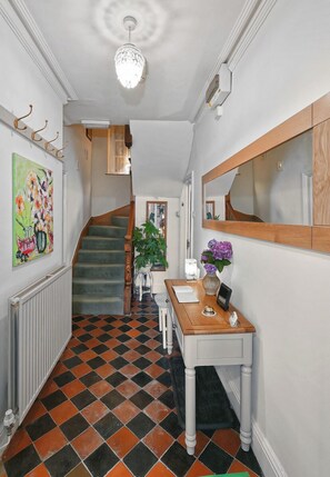 A hallway with a checkered floor, a staircase, a wooden desk with a mirror, and a radiator.