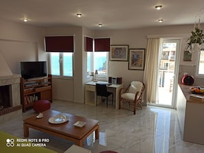 A living room with a TV, fireplace, dining table, and a view of the sea.