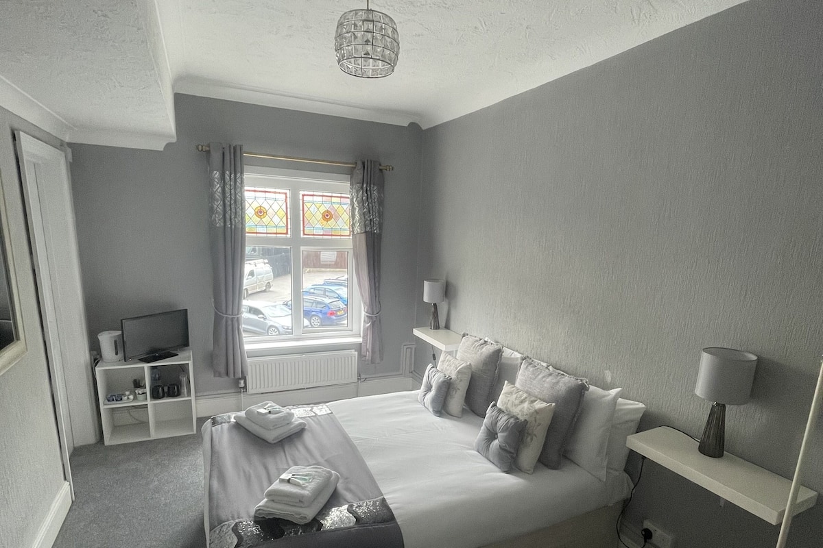 A bedroom with a bed, bedside tables, a lamp, a TV, and a window with curtains.