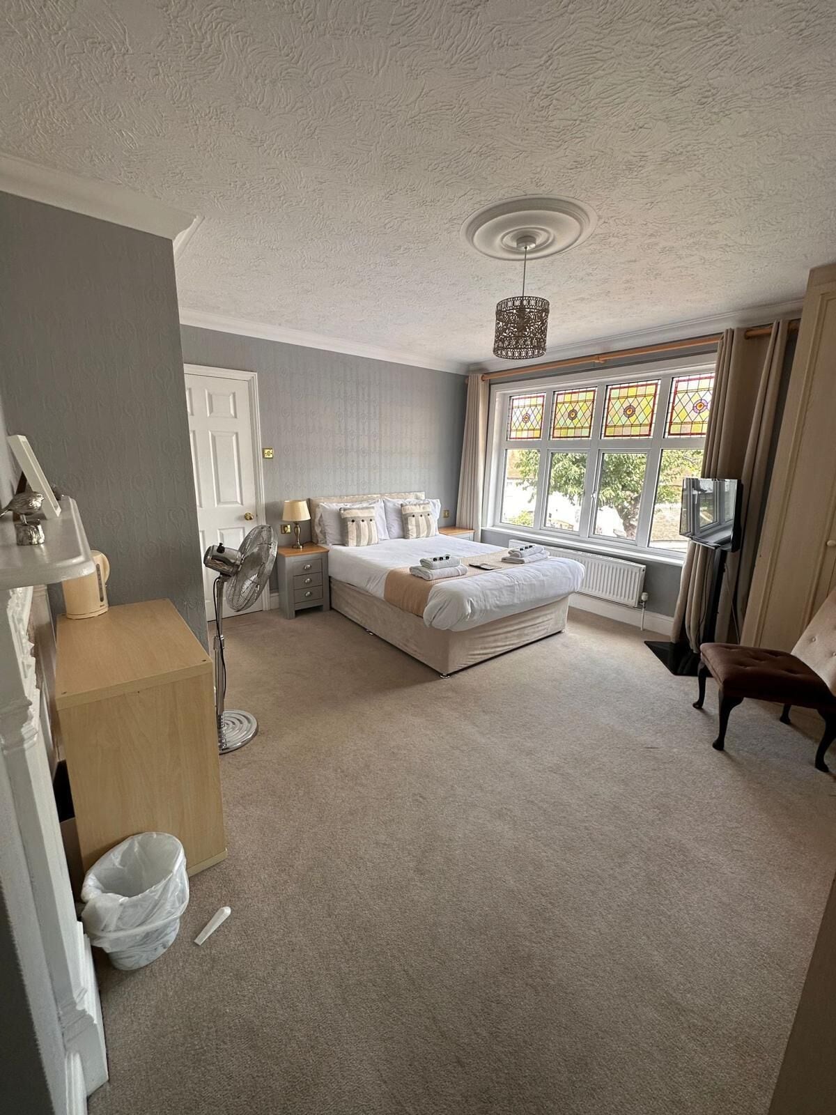 A bedroom with a bed, bedside tables, a radiator, a window with curtains, and a chair.