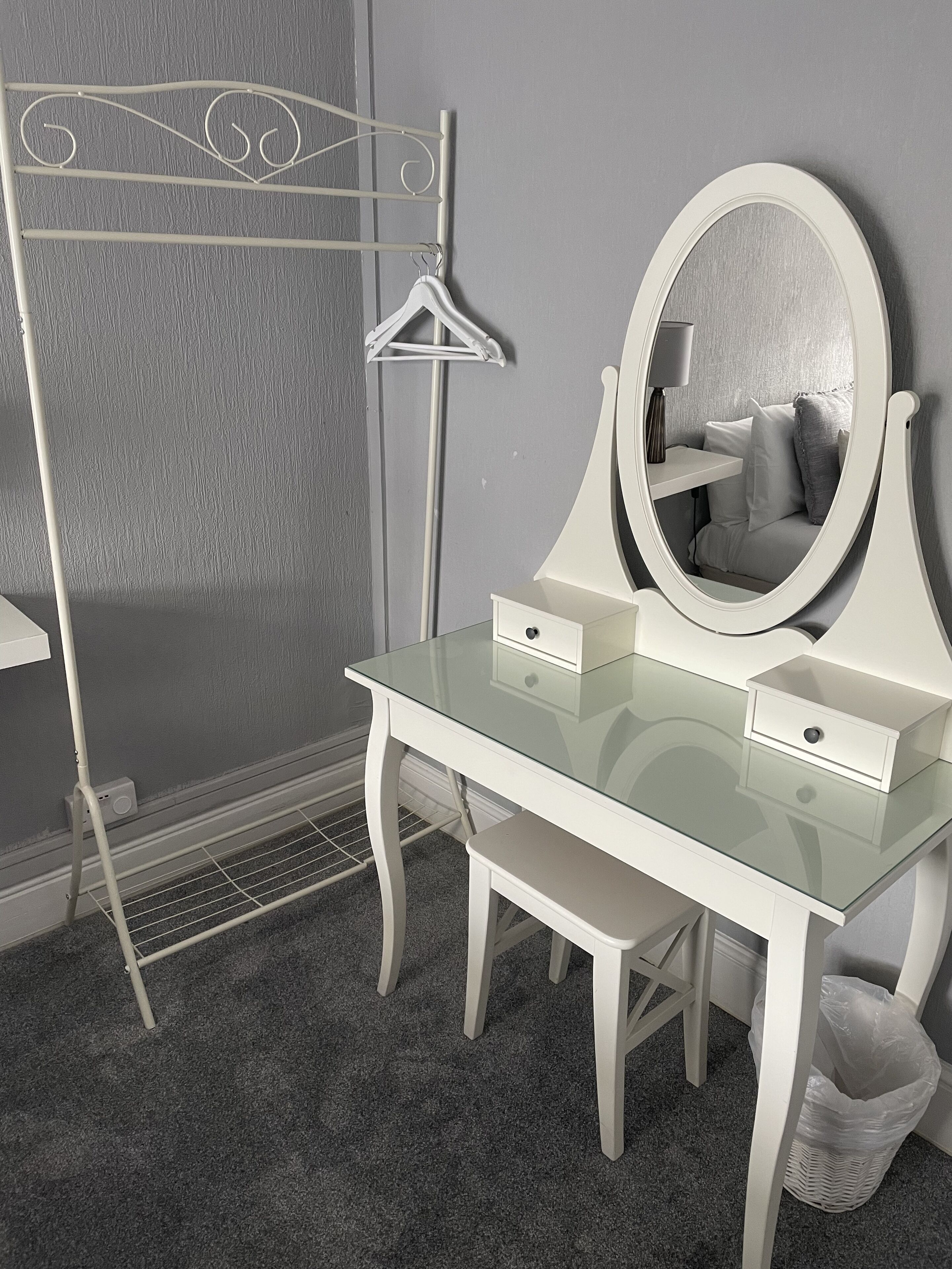 A white vanity with a glass top, a large mirror, and a small drawer.