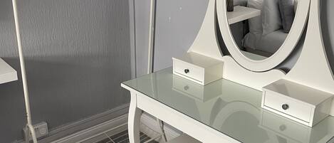 A white vanity with a glass top, a large mirror, and a small drawer.