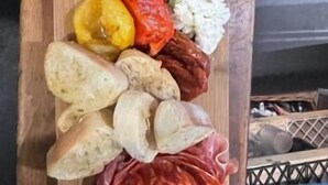 Un tagliere di legno con diversi cibi tra cui insalata, pane e salumi.